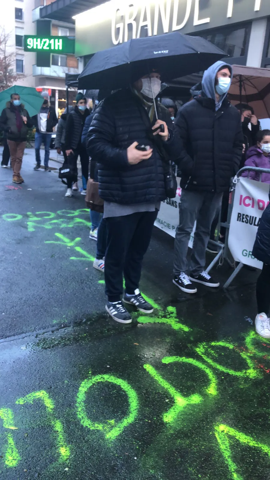 File d'attente sous la pluie devant une pharmacie pendant une vague COVID